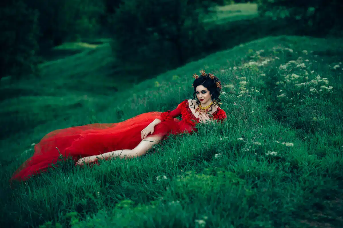 countess in a long red dress  is walking in a green forest full