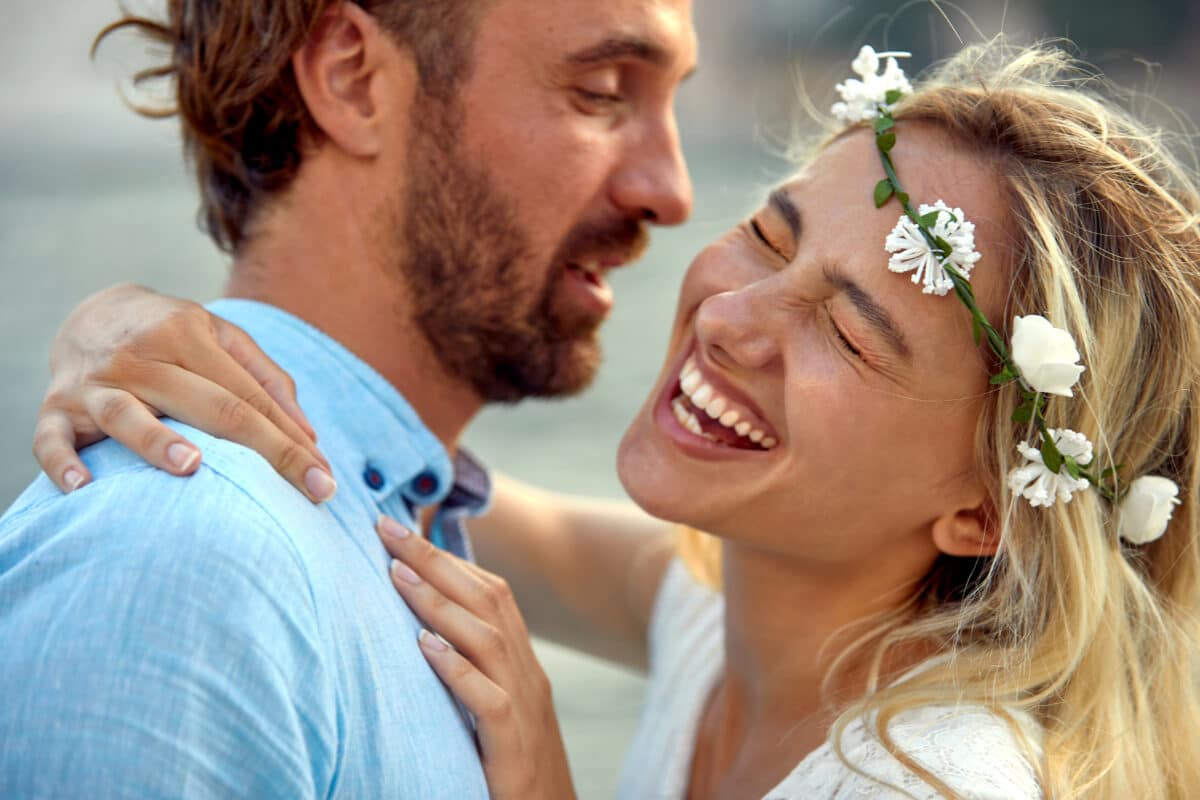 couple in love, happy woman with a flower head wreath hugs her lover by the sea