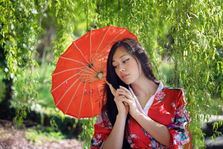 Beautiful oriental woman with Japanese parasol under the willow tree